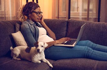 A woman on the couch with her dog using a laptop.