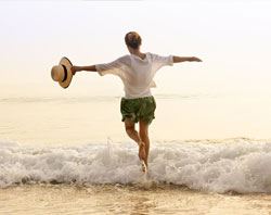 A lady holding her hat with her arms wide open playing in ocean water