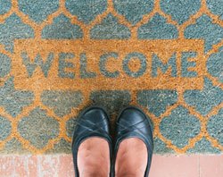 Pair of feet standing on a welcome mat.